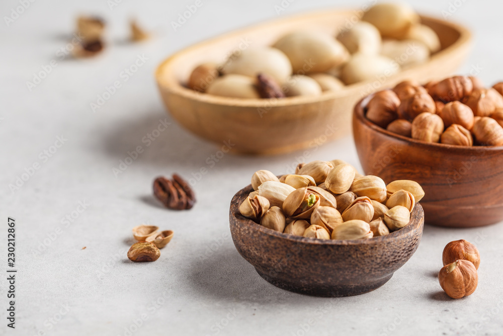 Pecans, hazelnuts and pistachios nuts in a wooden bowls on a white background. Pecans, hazelnuts and pistachios nuts in a wooden bowls on a white background.