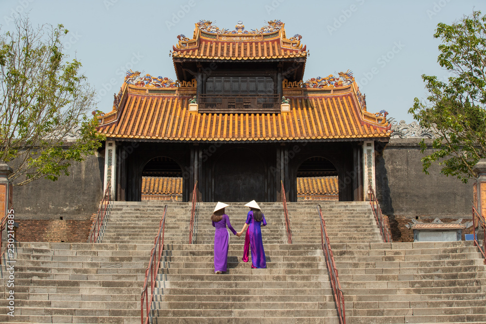 Fototapeta premium Traditionally dressed Vietnamese young women climb the stair of historical Khiem Cung Palace ( Tomb ).