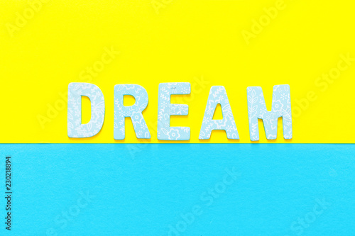 Word DREAM made out of small blue wooden letter on yellow and blue background, flat lay