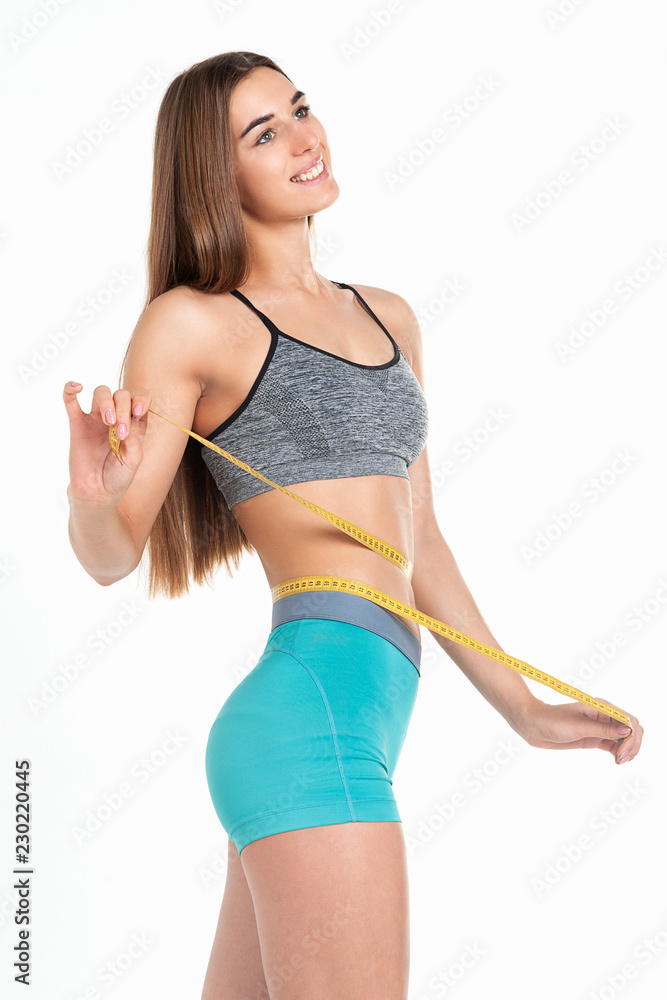 Fototapeta premium Diet concept. Perfectly slim girl measures her waist with a tape. Studio, white background. 