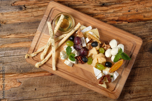 Cheese platter with assorted cheeses, grapes, olives, grissini and honey on the cutting bord