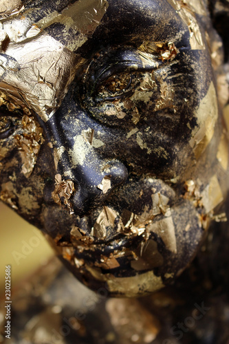 Close up of the face of a statue of a monk partially covered in gold leaf at a Buddhist temple in south east Asia. photo