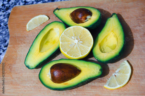 tasty ripe green avocado with brown bone and yellow lemon on a wooden board