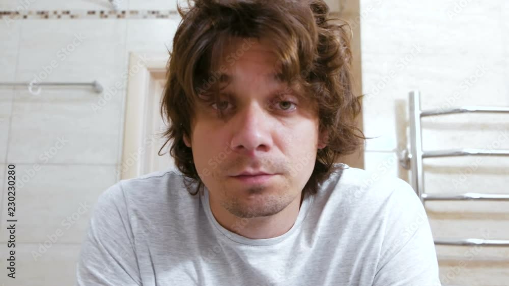 Sleepy shaggy young man looks at the mirror in bathroom in the morning and combs long hair with hands. Sleepy shaggy young man looks at the mirror in bathroom in the morning and combs long hair with hands.