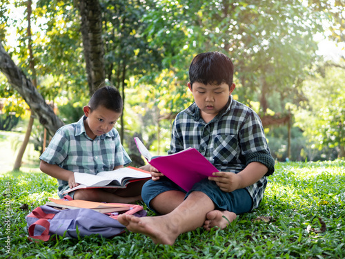 Cute two asian student boy reading book in the nature park with sunlight background, people, learning, relax, education and Natural classroom concept..