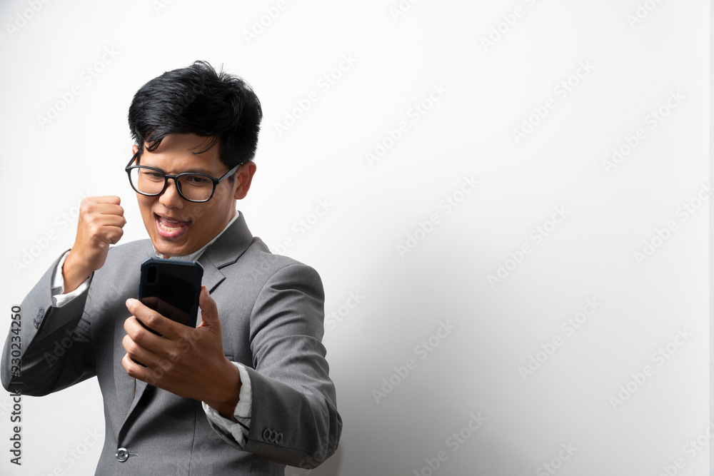 A business man is showing glad and success expression while looking at the smartphone on left hand and make a fist on righthand. More space. A business man is showing glad and success expression while looking at the smartphone on left hand and make a fist on righthand. More space.