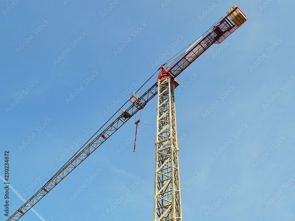 Tall construction tower crane against the blue sky on a day close up Tall construction tower crane against the blue sky on a day close up