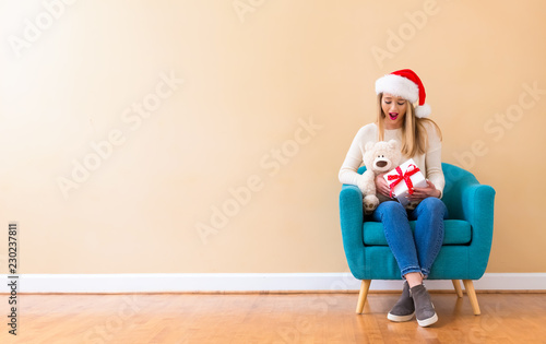 Young woman with santa hat holding a teddy bear in a chair