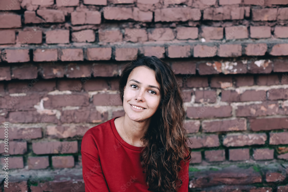  young fashionable girl in a red dress on a brick wall background.