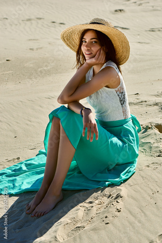 Young girl in a green skirt and hat posing against the background of sand