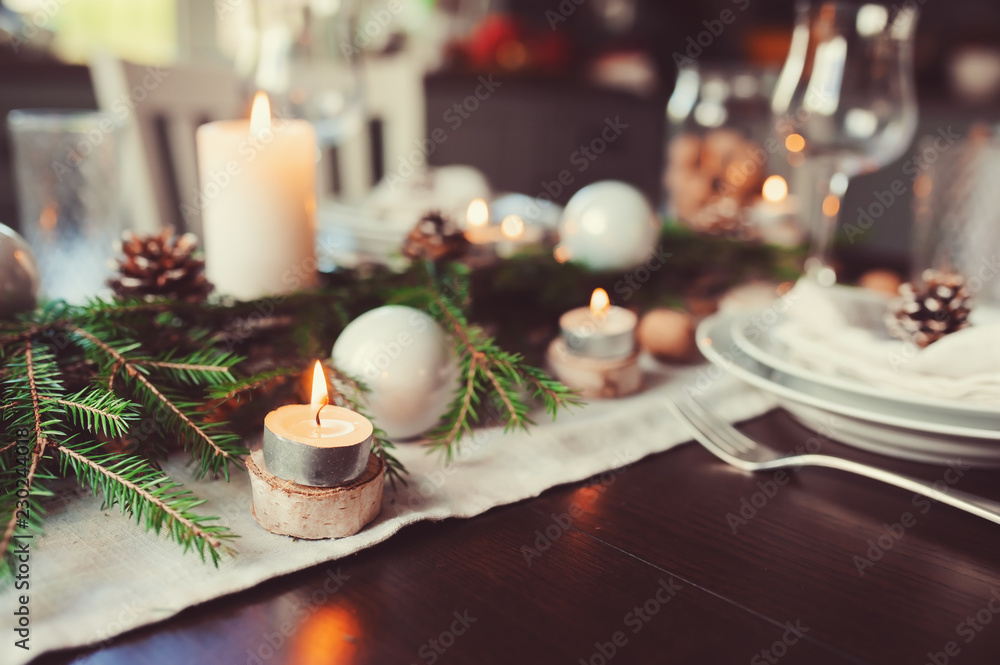 Festive Christmas and New Year table setting in scandinavian style with rustic handmade details in natural and white tones. Dining place decorated with pine cones, branches and candles Festive Christmas and New Year table setting in scandinavian style with rustic handmade details in natural and white tones. Dining place decorated with pine cones, branches and candles