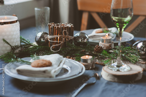 Festive Christmas and New Year table setting in scandinavian style with rustic handmade details in natural and white tones. Dining place decorated with pine cones  branches and candles