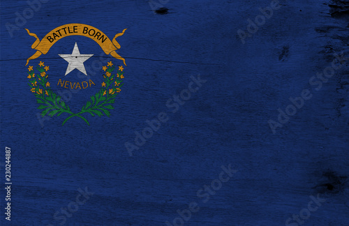 Flag of Nevada on wooden plate background. Grunge Nevada flag texture, The states of America. Solid cobalt blue field. The canton contains two sagebrush branches encircling a silver star.