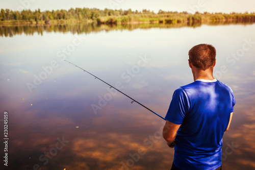 Young man fishing on river bank. Fisherman enjoying hobby. Spinning