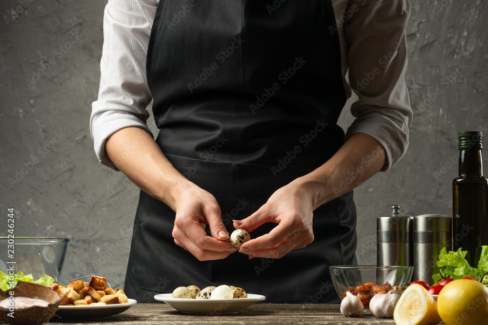 Chef cleans quail eggs for a vegetarian salad with seafood on the background of a concrete wall