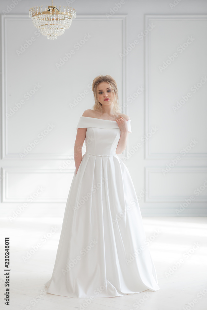 Young beautiful bride wearing white wedding dress in light classic studio interior. Vertical full-lenght portrait Young beautiful bride wearing white wedding dress in light classic studio interior. Vertical full-lenght portrait