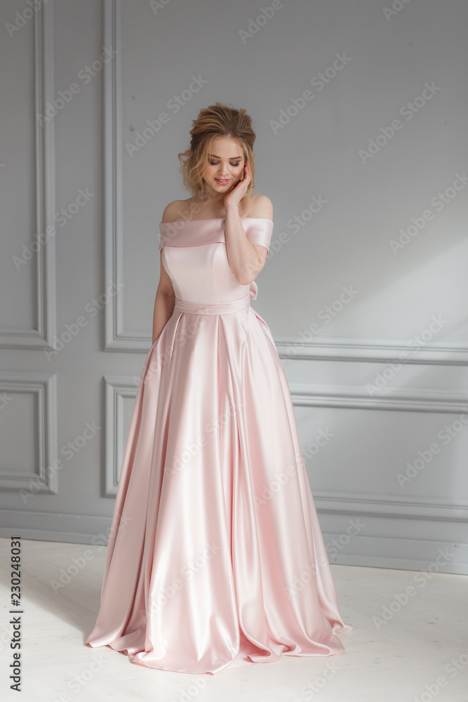 Full-lenght portrait of bride in beige silk wedding dress posing on gray wall background. Looking down Full-lenght portrait of bride in beige silk wedding dress posing on gray wall background. Looking down