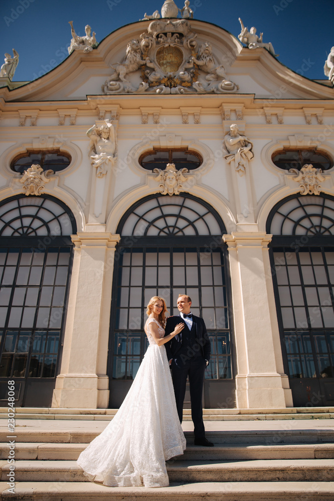 Groom and bride stand on stairs by the great palace in Wiena. Stylish couple