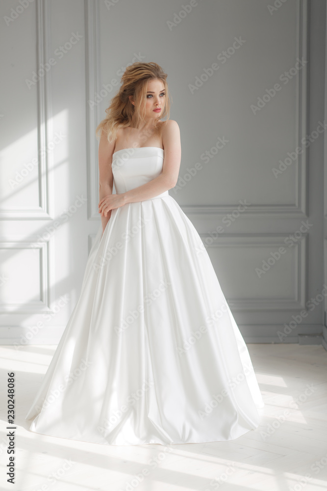 Beautiful blonde woman in beige powdery silk wedding dress posing in studio room Beautiful blonde woman in beige powdery silk wedding dress posing in studio room