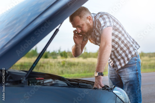 man with a phone in front of the open hood of a broken car