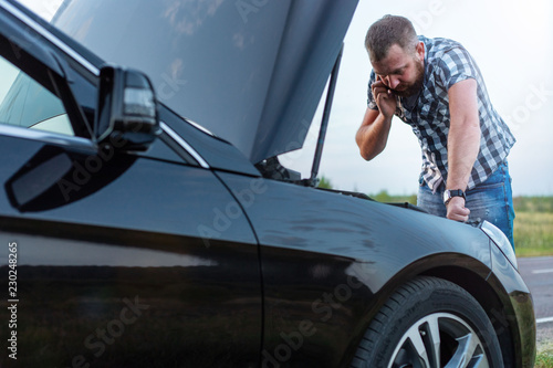 man with a phone in front of the open hood of a broken car