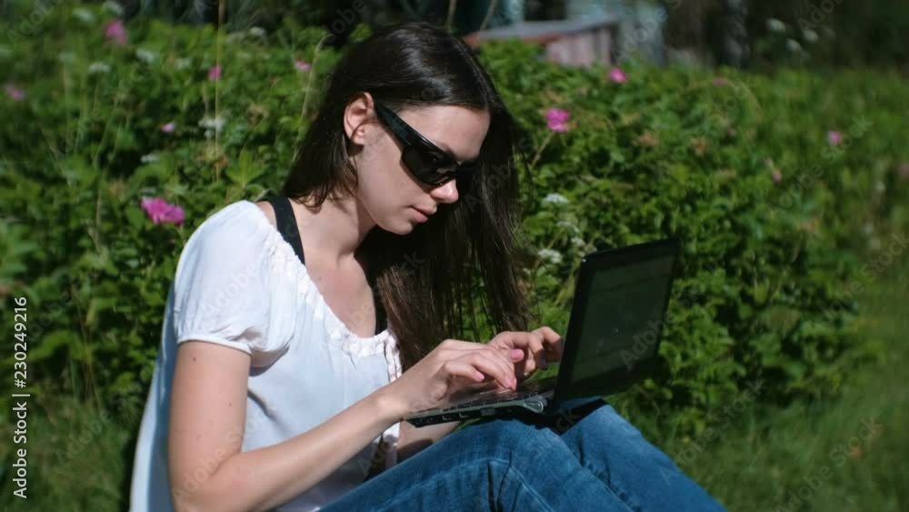 Beautiful brunette girl working typing on laptop sitting in Park in summer. Beautiful brunette girl working typing on laptop sitting in Park in summer.