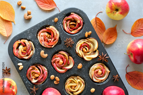 Tray of apple roses baked in puff pastry on gray concrete background with Autumn leaves and apples photo