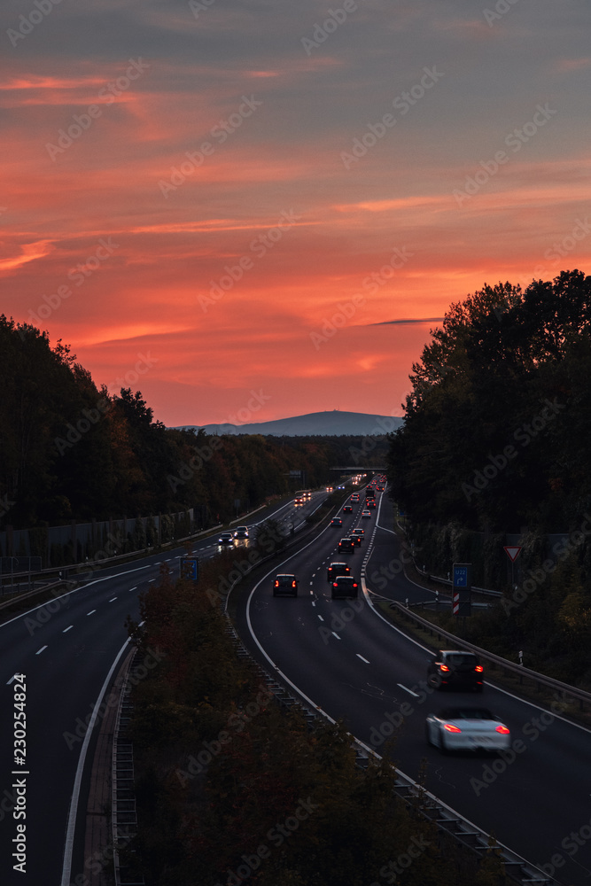 Straight lines view of a traffic german autobahn highway in the evening colorful sunset light with mountain view in the background. Driving in the evening