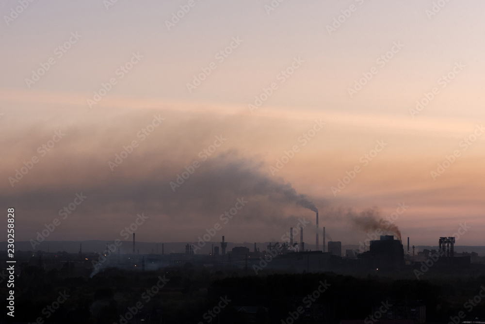 Large pipes of the plant pollute emissions environment at sunset