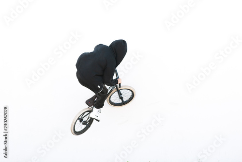 Rider's back in dark clothes riding a white wall on a bmx bike. bmx trick on a white background. Copyspace