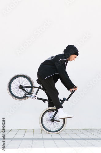 Bmx racer makes a trick in against the background of a white wall. Bmx rider with a bicycle in flight on a white background. Street bmx freestyle. Copyspace