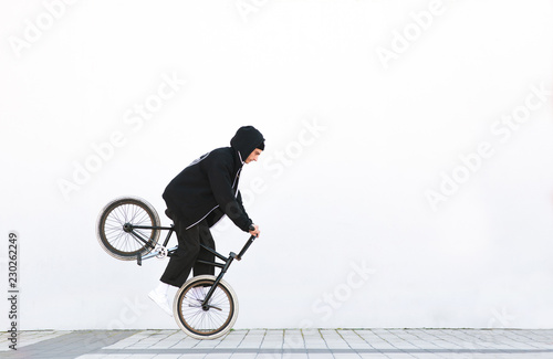 Bmx racer makes a trick in against the background of a white wall. Bmx rider with a bicycle in flight on a white background. Street bmx freestyle. Copyspace