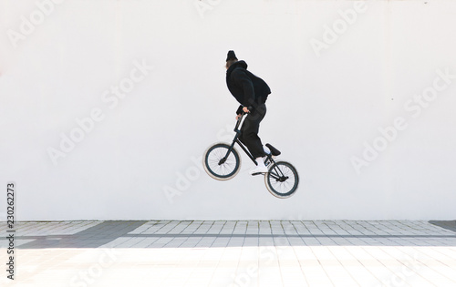 Young man in casual clothing makes a trick on a bmx bike. Bmx freestyle on the background of a white wall