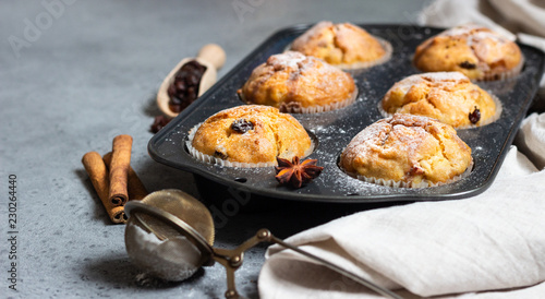 Fresh homemade apple cinnamon muffins in black baking dish with raisins, cinnamon sticks and anise.