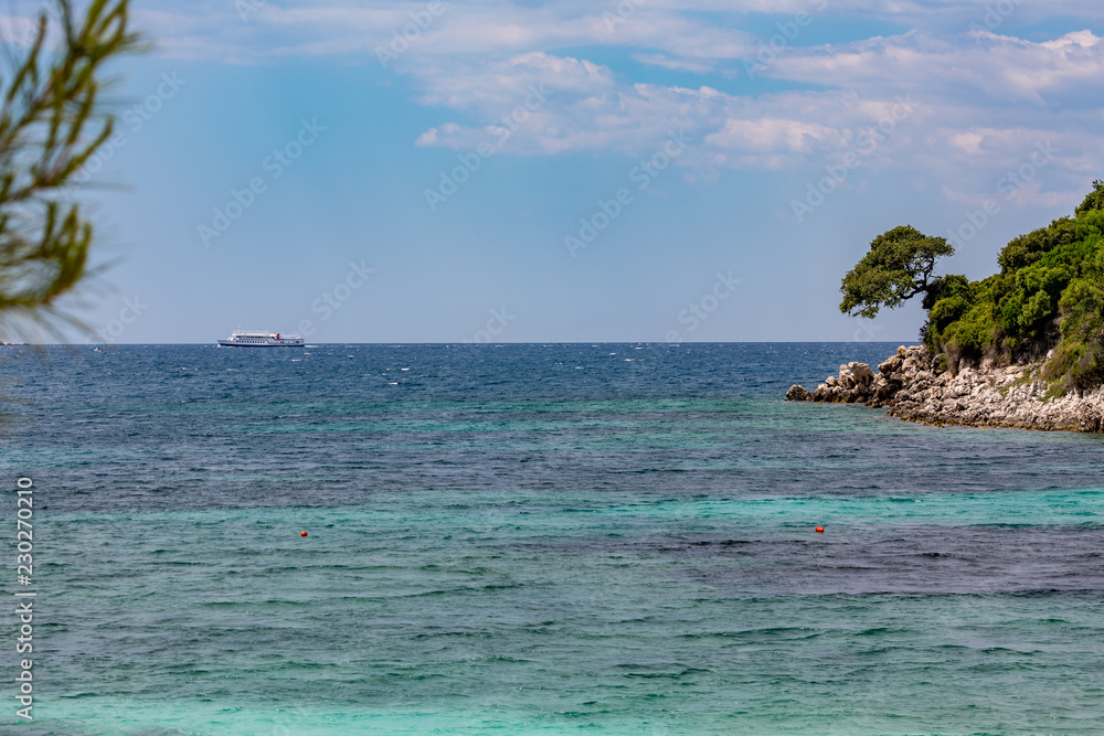 Spring daytime beautiful Ionian Sea with clear turquoise water, rocks and trees coast view from Ksamil beach, Albania. Deep blue sky with white clouds.