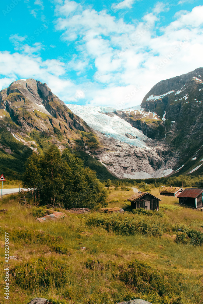 Blick auf einen Gletscher in Norwegen mit Holzhütten im Vordergrund / View at a glacier in norway with cabins in the foreground