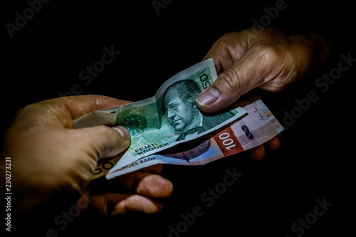 Photography Two hands handing over Norwegian kroner banknotes to each other