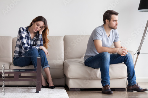 Sad, desperate, frustrated young couple no desire to talk after quarrel. Man sitting with back to wife, thinking of relationship problems. Troubles in family, misunderstanding, distrust