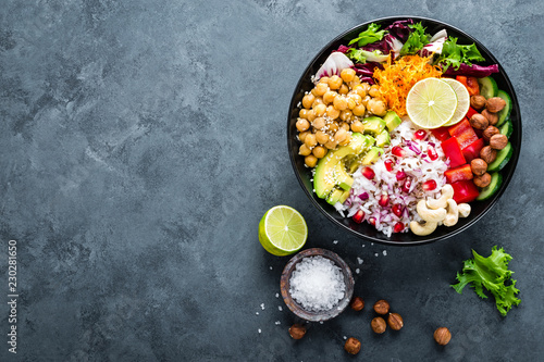 Healthy vegetarian Buddha bowl with fresh vegetable salad, rice, chickpea, avocado, sweet pepper, cucumber, carrot, pomegranate and nuts closeup photo