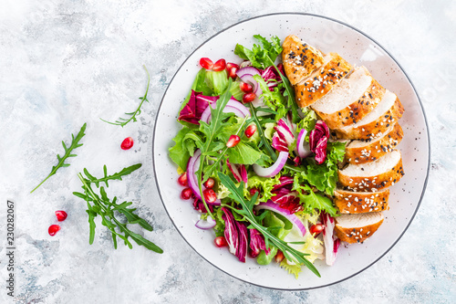 Grilled chicken breast, fillet and fresh vegetable leafy salad with arugula and pomegranate on plate