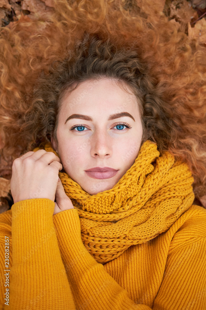 Redhead curly cheerful cute girl liying in the autumn leaves, holding scarf Redhead curly cheerful cute girl liying in the autumn leaves, holding scarf