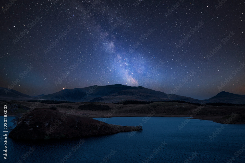 Vibrant Milky Way composite image over landscape of Llyn y Dywarchen lake in Snowdonia National Park