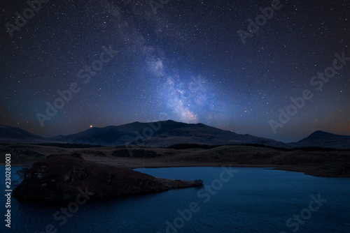 Vibrant Milky Way composite image over landscape of Llyn y Dywarchen lake in Snowdonia National Park