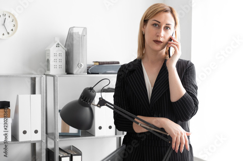 A young girl in the office talking on the phone and put her hand on the high lamp. photo