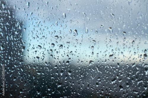 Cold shiny drops of autumn rain on the window pane in rainy autumn weather. Cool background with a sad quiet mood. Crying rain on the glasses.