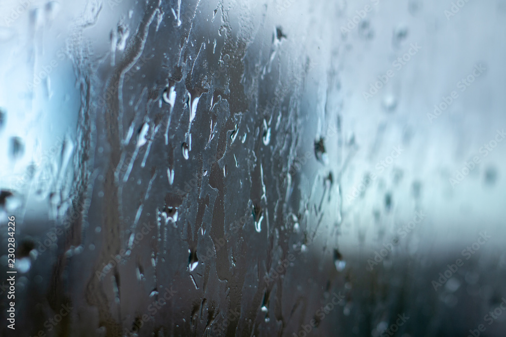 Blurred photo of cold autumn rain drops on the window pane in rainy autumn weather. Cool background with a sad quiet mood. Crying rain on the window glasses. Blurred photo of cold autumn rain drops on the window pane in rainy autumn weather. Cool background with a sad quiet mood. Crying rain on the window glasses.