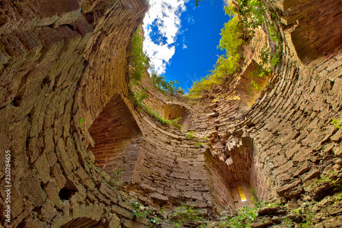 A look up from a medieval round stone tower without a roof, grass grows from the yellow walls, a blue sky with clouds. Koporye Fortress, Leningrad District, Saint Petersburg, Russia. photo