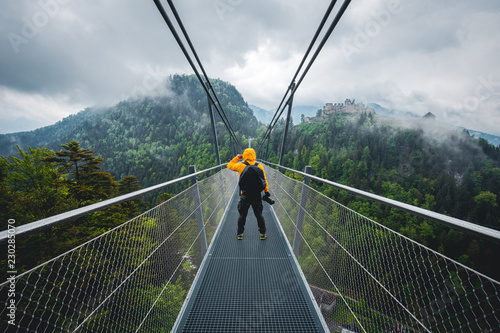 Man with yellow coat and camera standing on the bridge