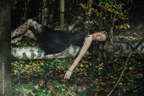 A young kind witch in a black dress with a black mask in a mystical forest in various poses. Art processing photo