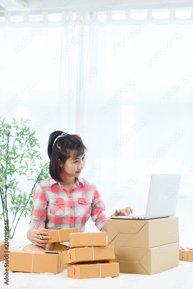 Woman small business owner, business start up in bedroom, young entrepreneur work with laptop prepare parcel boxes for deliver to customer Woman small business owner, business start up in bedroom, young entrepreneur work with laptop prepare parcel boxes for deliver to customer